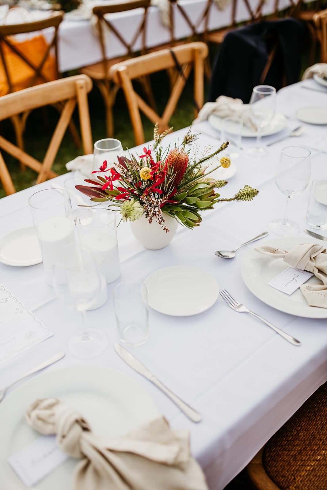 Decorative table setting with native flowers, plates, and cutlery on a white tablecloth.
