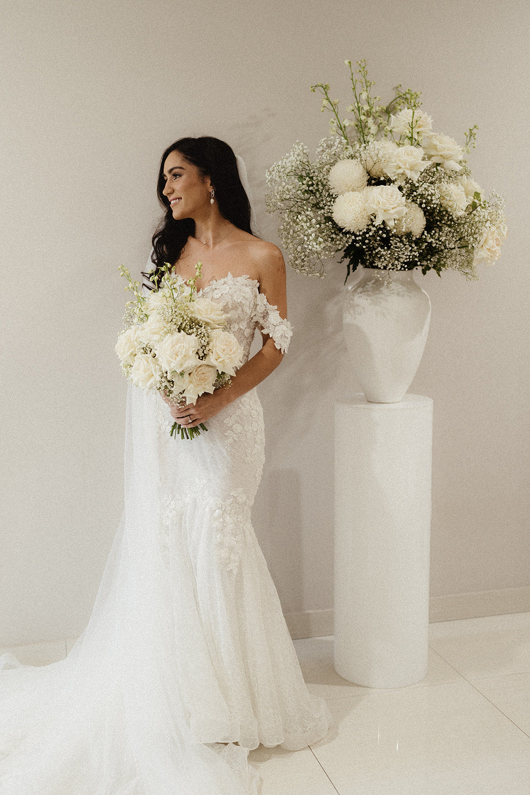 The bride in an off-the-shoulder lace gown holding her white floral bouquet
