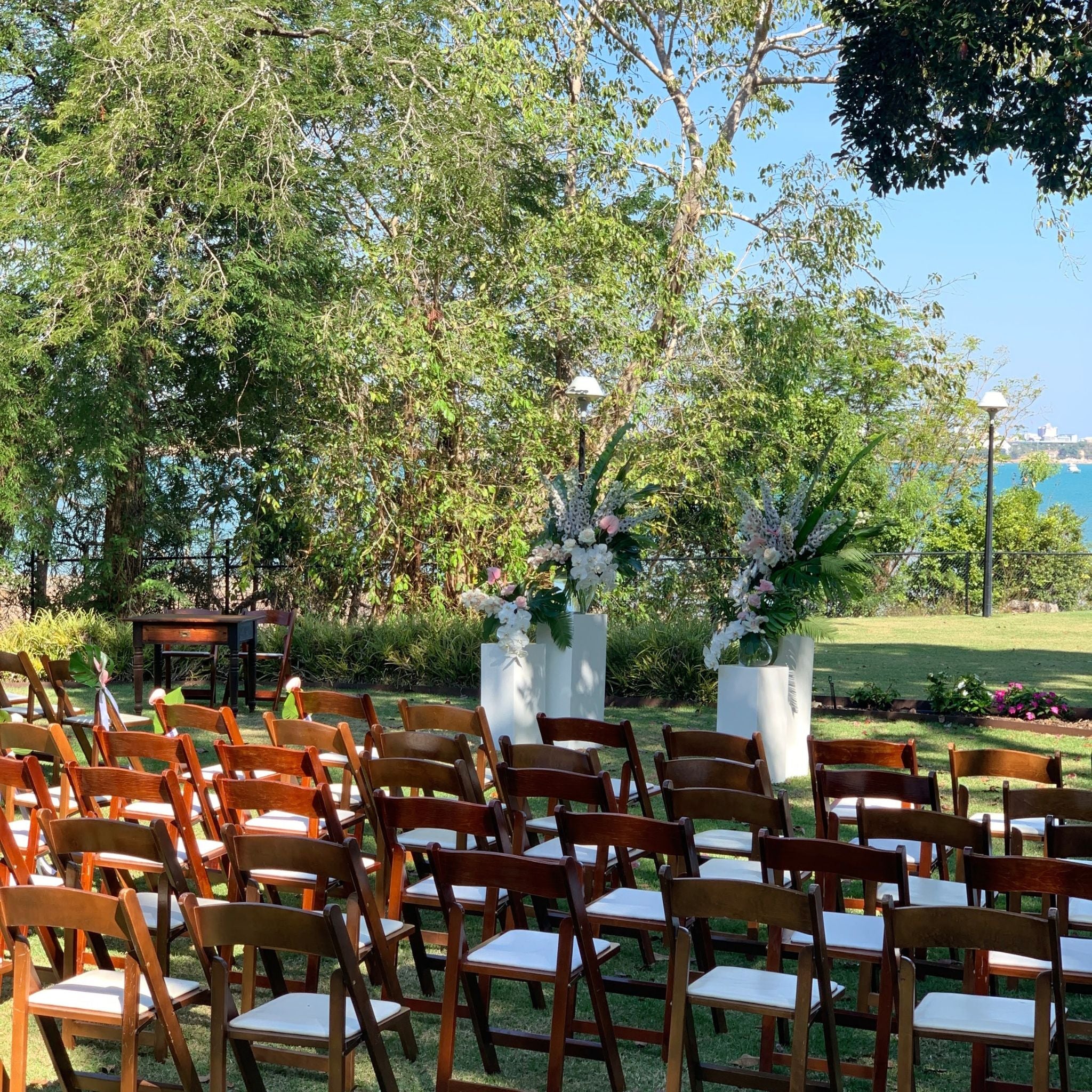 Wedding ceremony with white plinths and vases of delphinium in white and soft pinks with tropical accents from anthuriums overlooking the water at Pee Wees at the Point