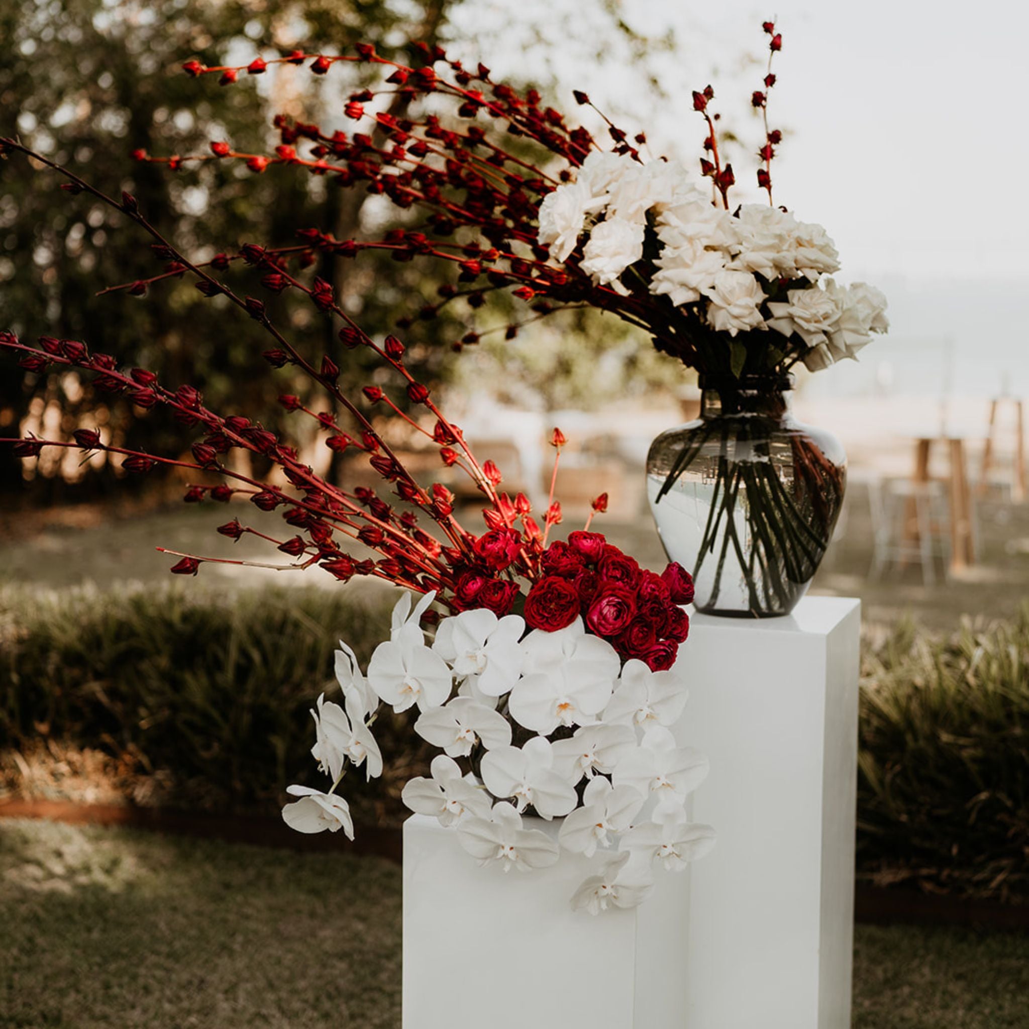White plinths with smoke vases topped with Darwin grown rosellas, roses and orchids