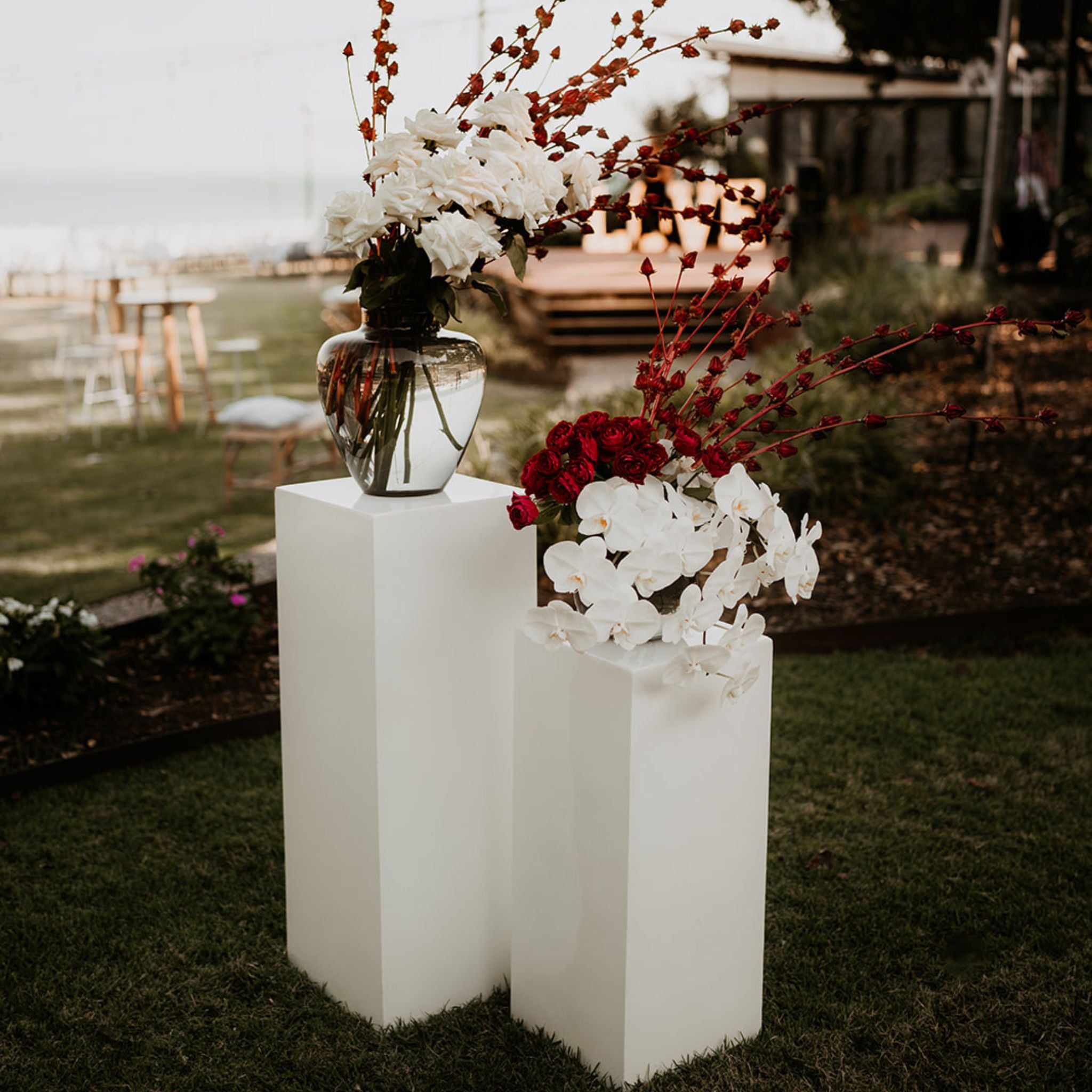 White plinths with smoke vases topped with Darwin grown rosellas, roses and orchids