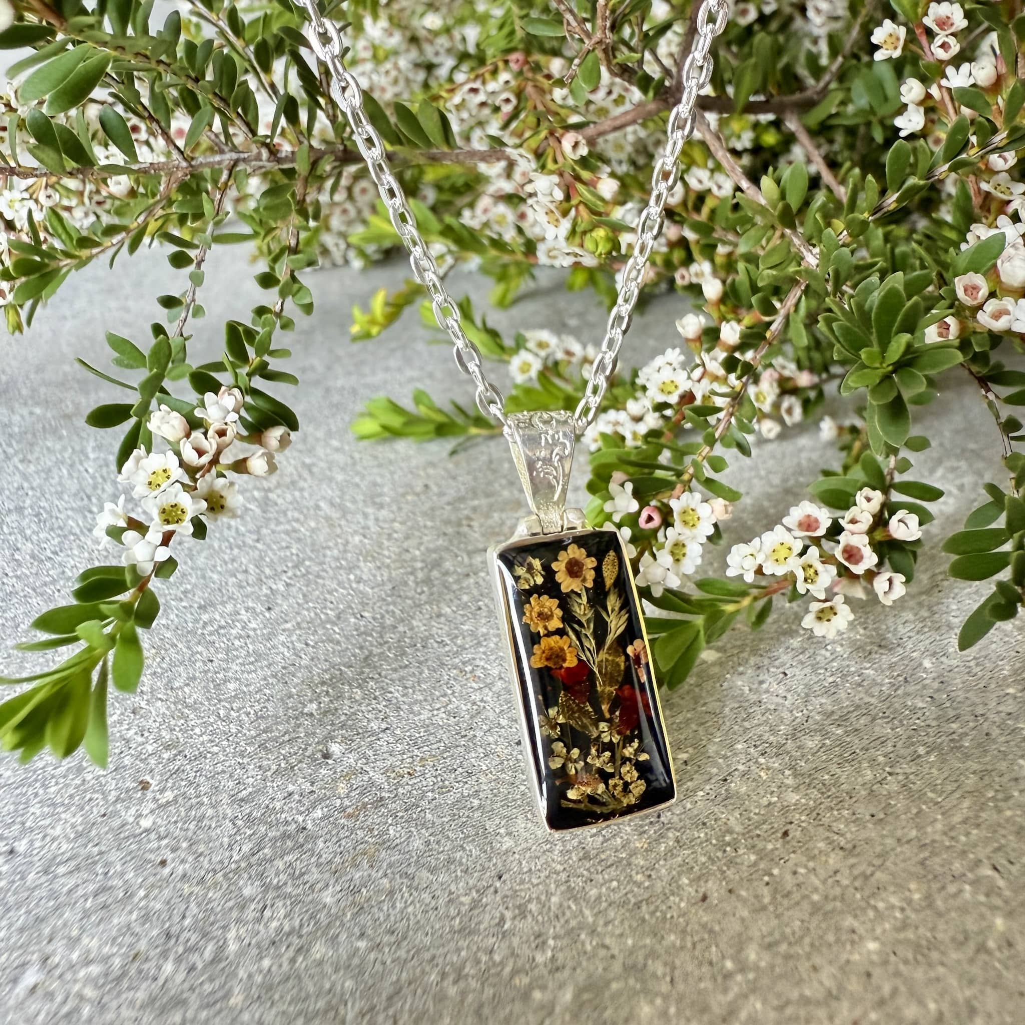 Necklace with a rectangular pendant featuring pressed flowers on a silver chain.