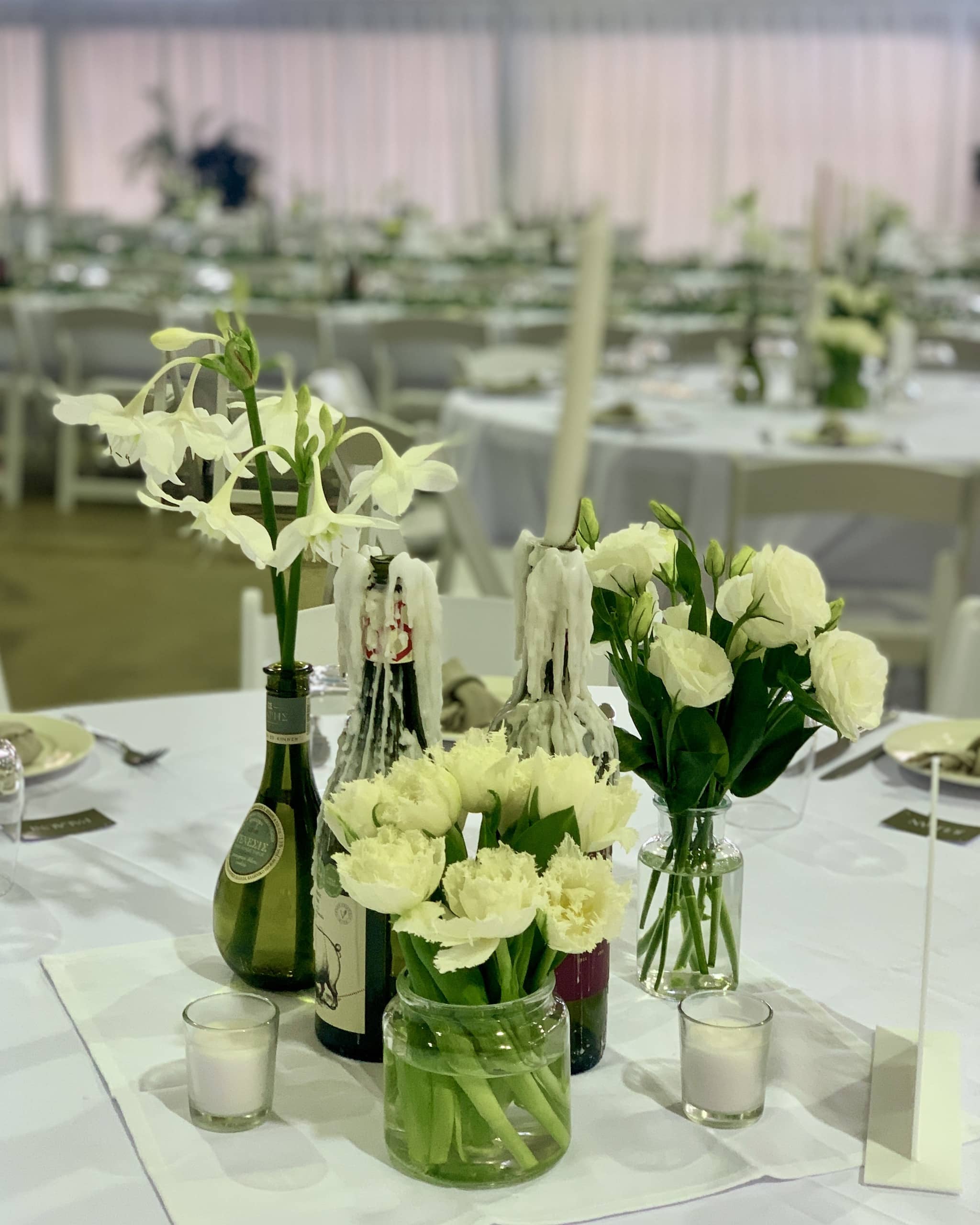 Wedding centrepiece with a cluster of flower filled bottles and candles Beija Flor Darwin florist