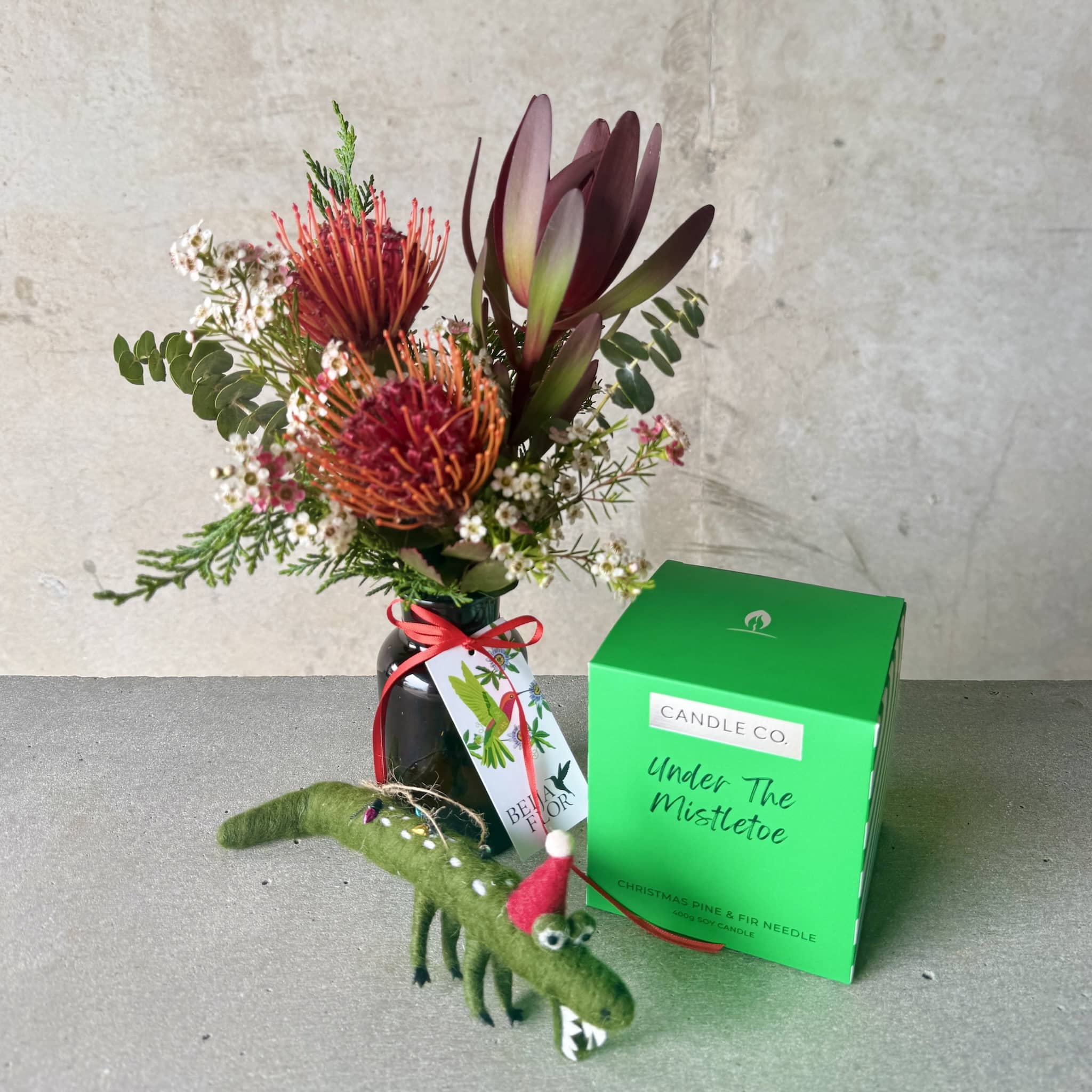 Floral arrangement with a small green crocodile ornament and an 'Under The Mistletoe' candle