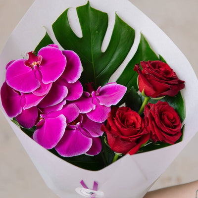 Close up red rose and orchid bouquet with monstera leaf