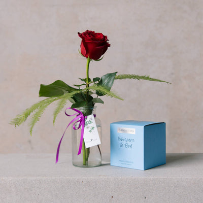 Red rose in a glass vase with monstera leaf and fern, scented candle in a box. 